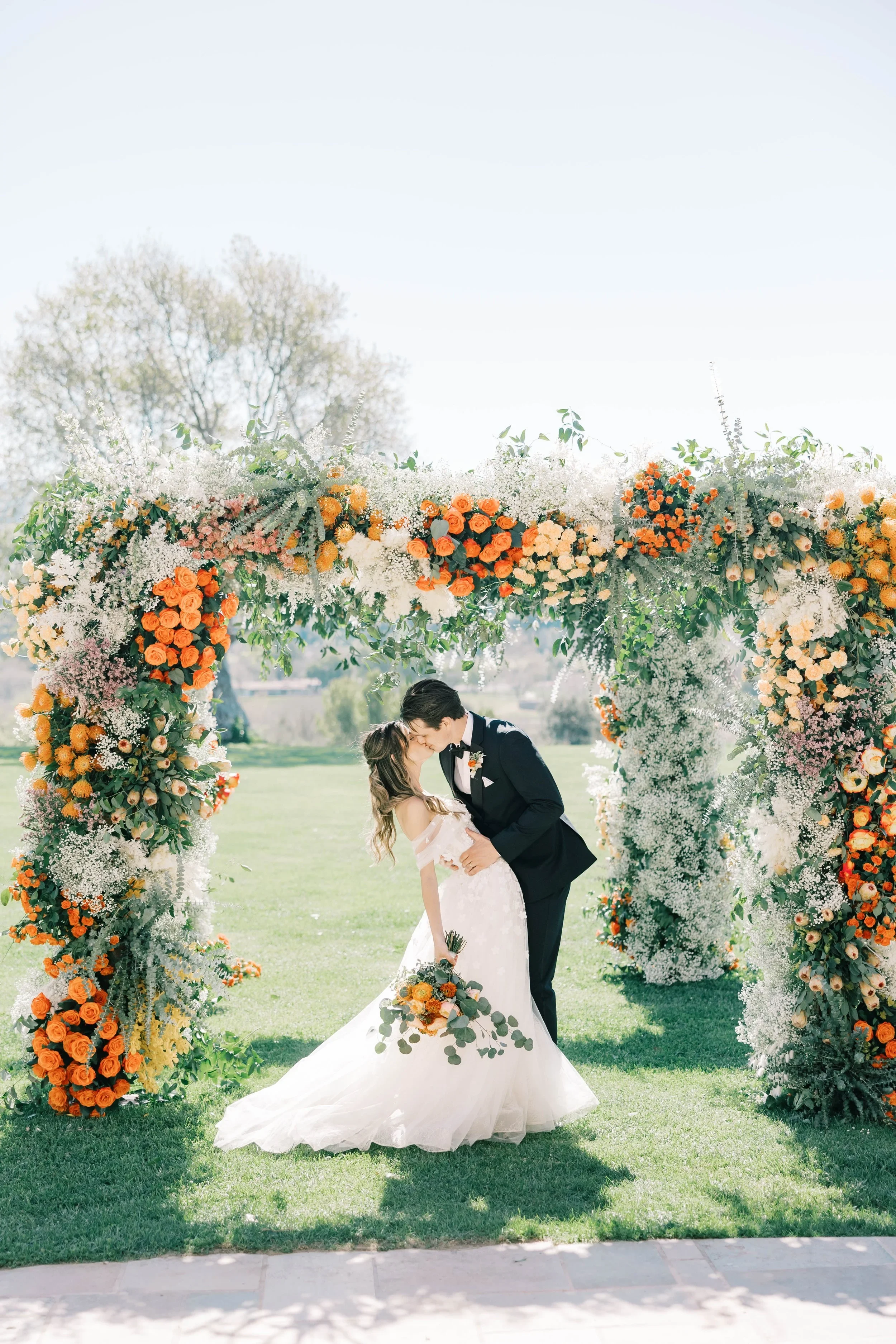 Couple under a chuppah with orange and white florals